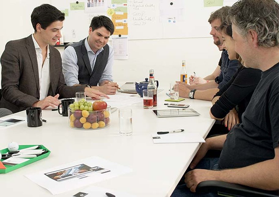 Beratungs-Situation mit 5 Personen an einem Tisch sitzend. 