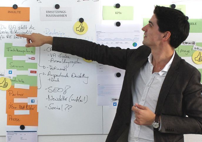 Workshop-Situtation in der eine Person etwas an einem Whiteboard erklärt.